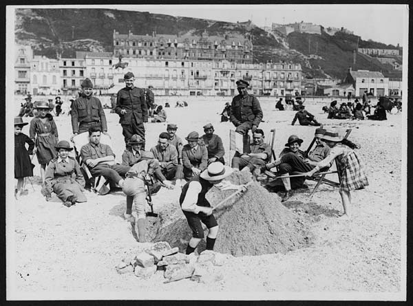 (29) N.420 - British, French and American soldiers seated with W.A.A.C.s on the sands watching French kiddies building sand castles