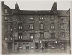 View of a street of three storey tenement buildings with shops on the ground floor